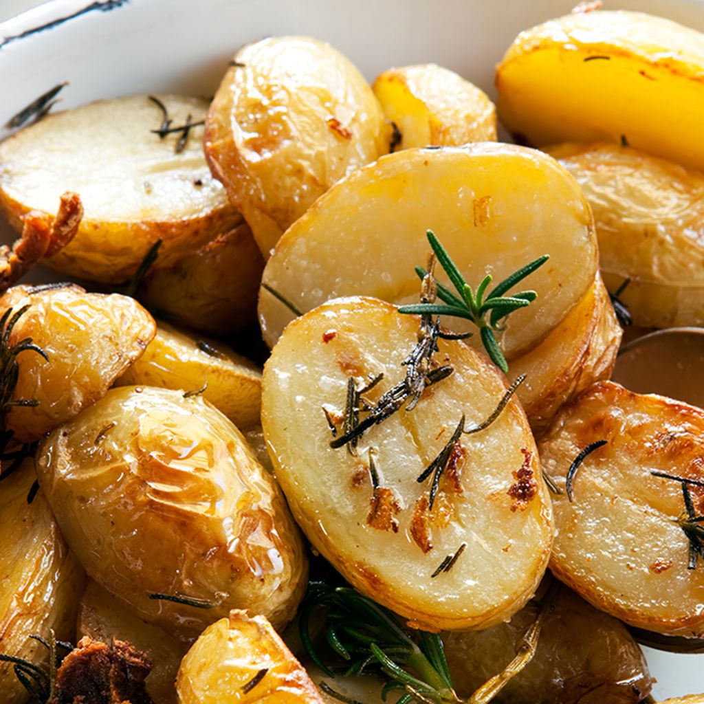 Crispy, halved golden roasted potatoes seasoned with fresh rosemary sprigs in a white serving dish.