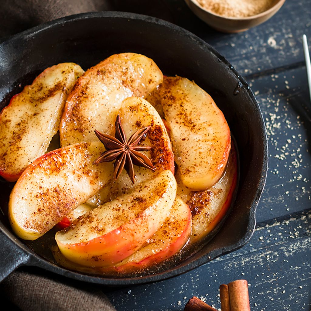 Sliced apples dusted with cinnamon and topped with star anise in a black cast-iron skillet.