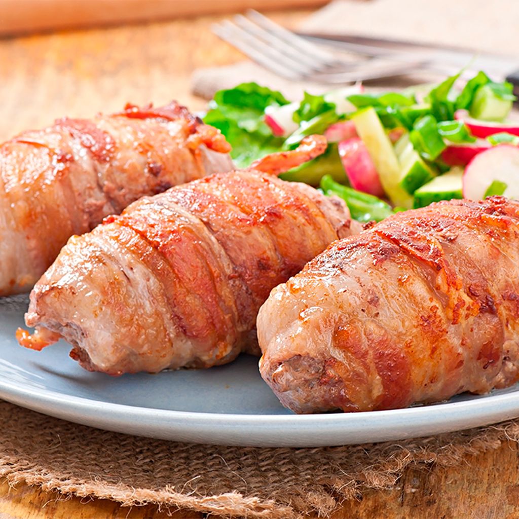Three grilled pork neck rolls wrapped in crispy bacon, served on a light blue plate with a fresh radish and green salad.