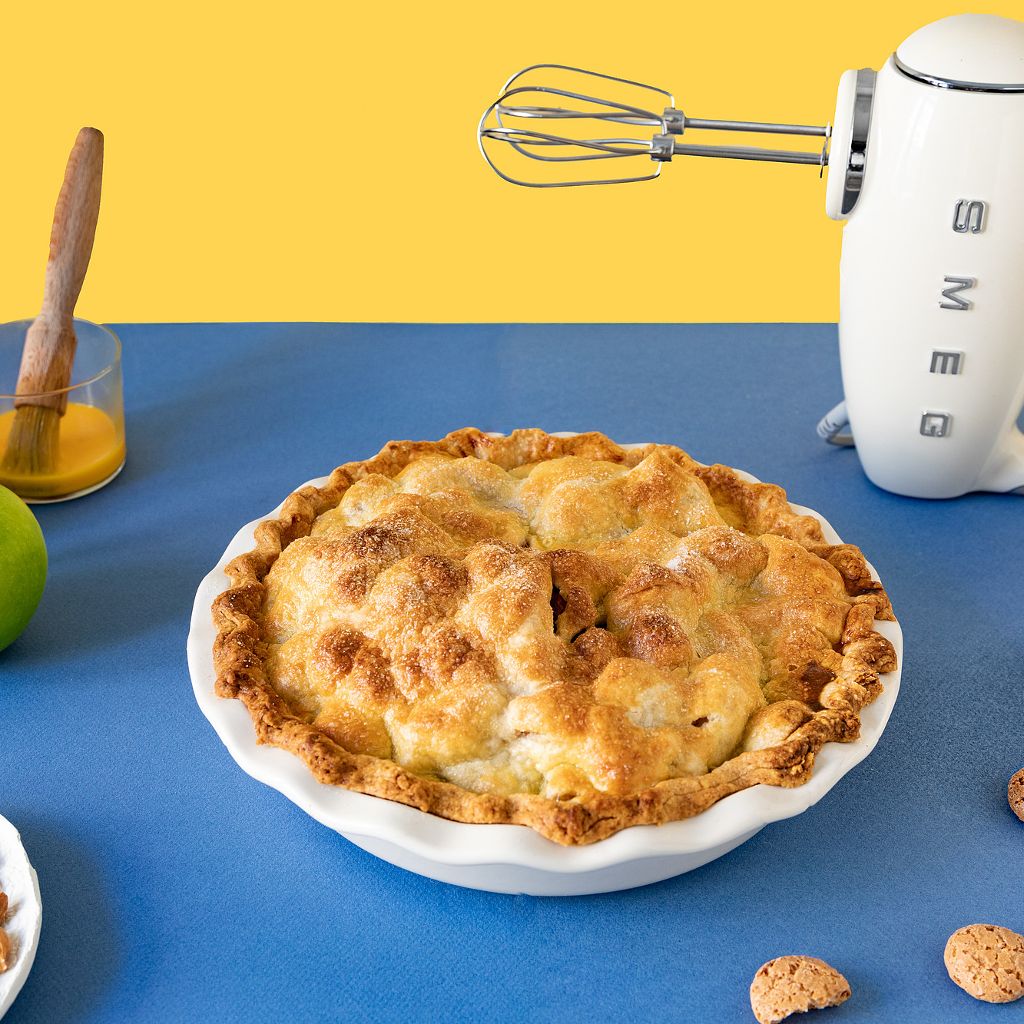 Slices of apple pie with a golden crust and almond topping on white plates with a silver server and blue napkin.