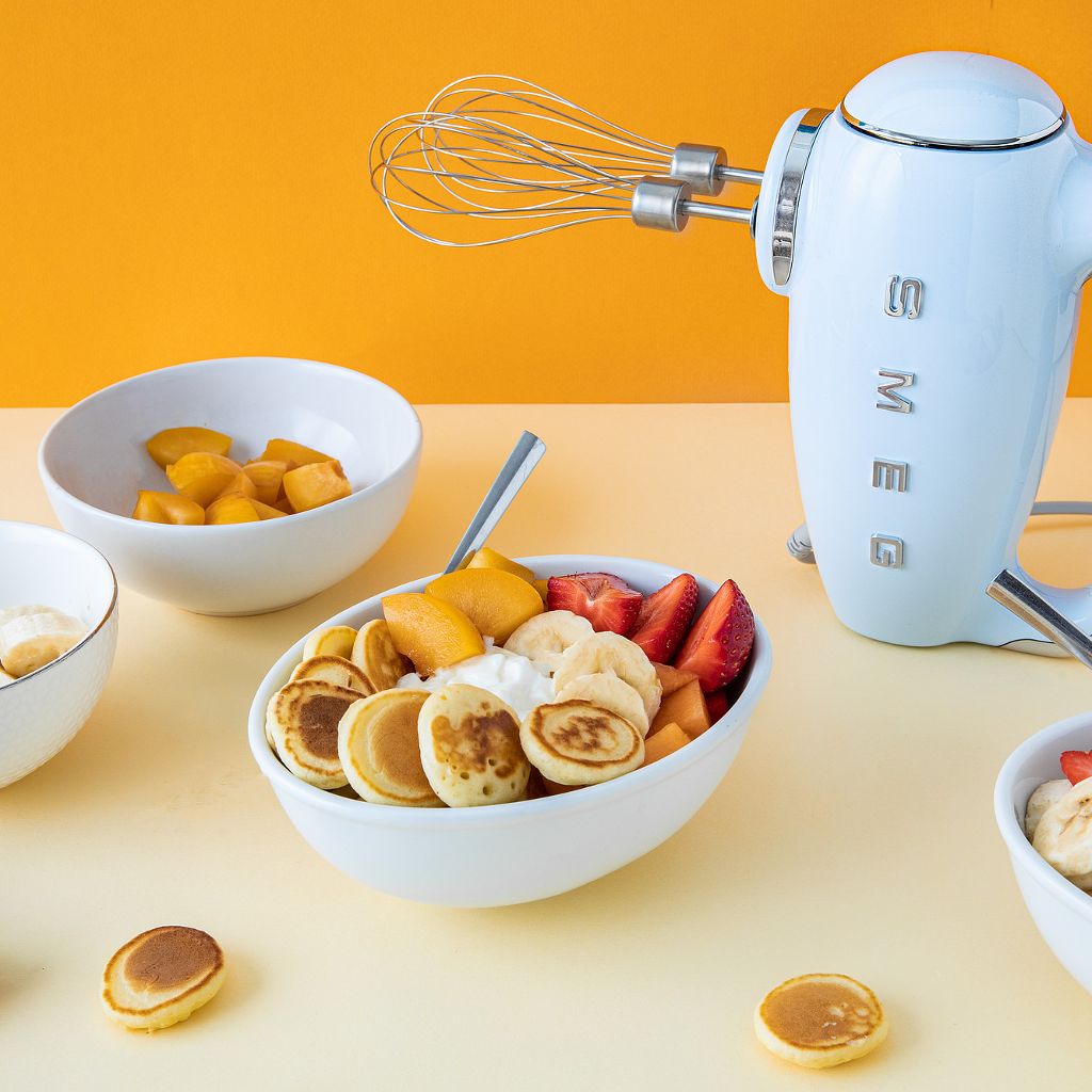 A pastel blue Smeg kettle next to bowls of mini pancakes topped with fresh strawberries, bananas, and syrup.