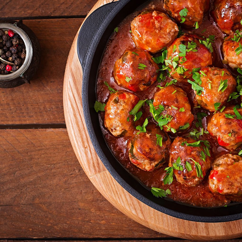A top-down view of savory meatballs simmered in a rich tomato sauce, garnished with fresh herbs in a black pan.