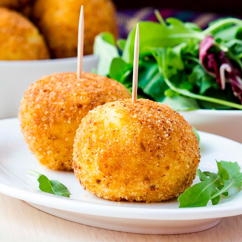 Two golden-fried mozzarella balls with toothpicks on a white plate, served with a fresh green side salad.