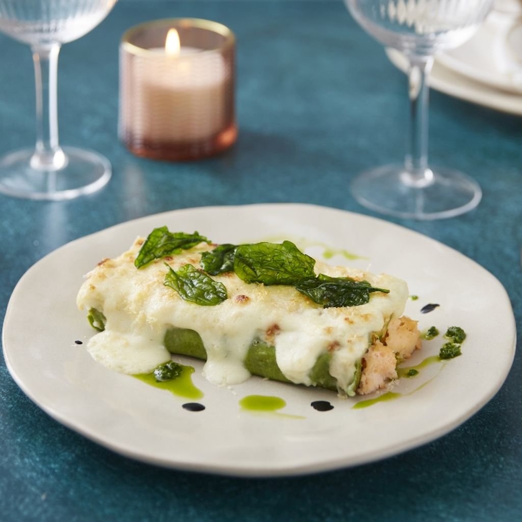 Green cannelloni rolls filled with salmon, covered in melted white sauce and topped with crispy sage.