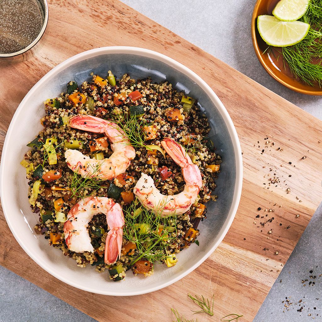 Quinoa bowl with grilled shrimp, vegetables, and herbs served on a wooden board with lime wedges