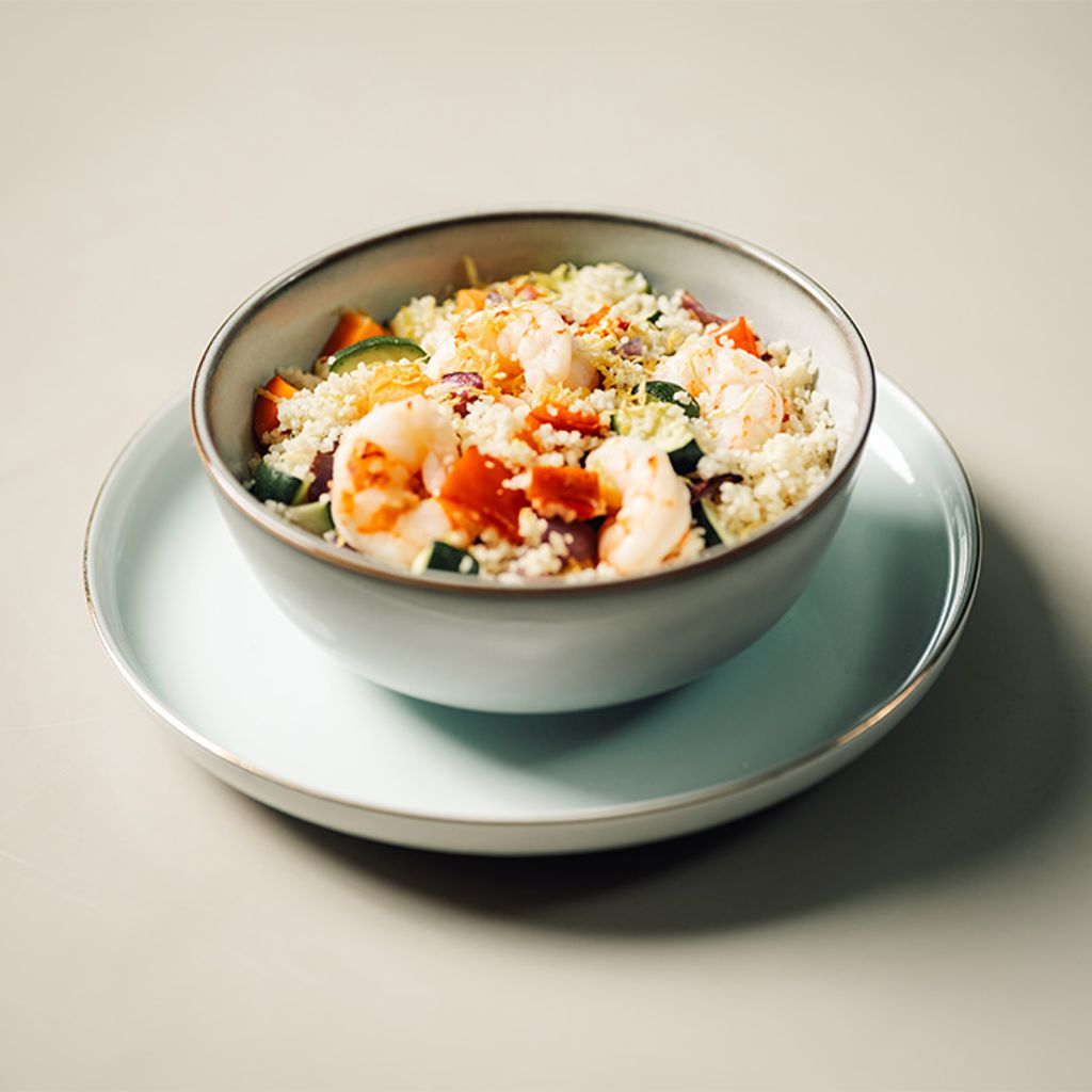 Bowl of couscous with shrimp, vegetables and grated cheese served on a minimalist plate