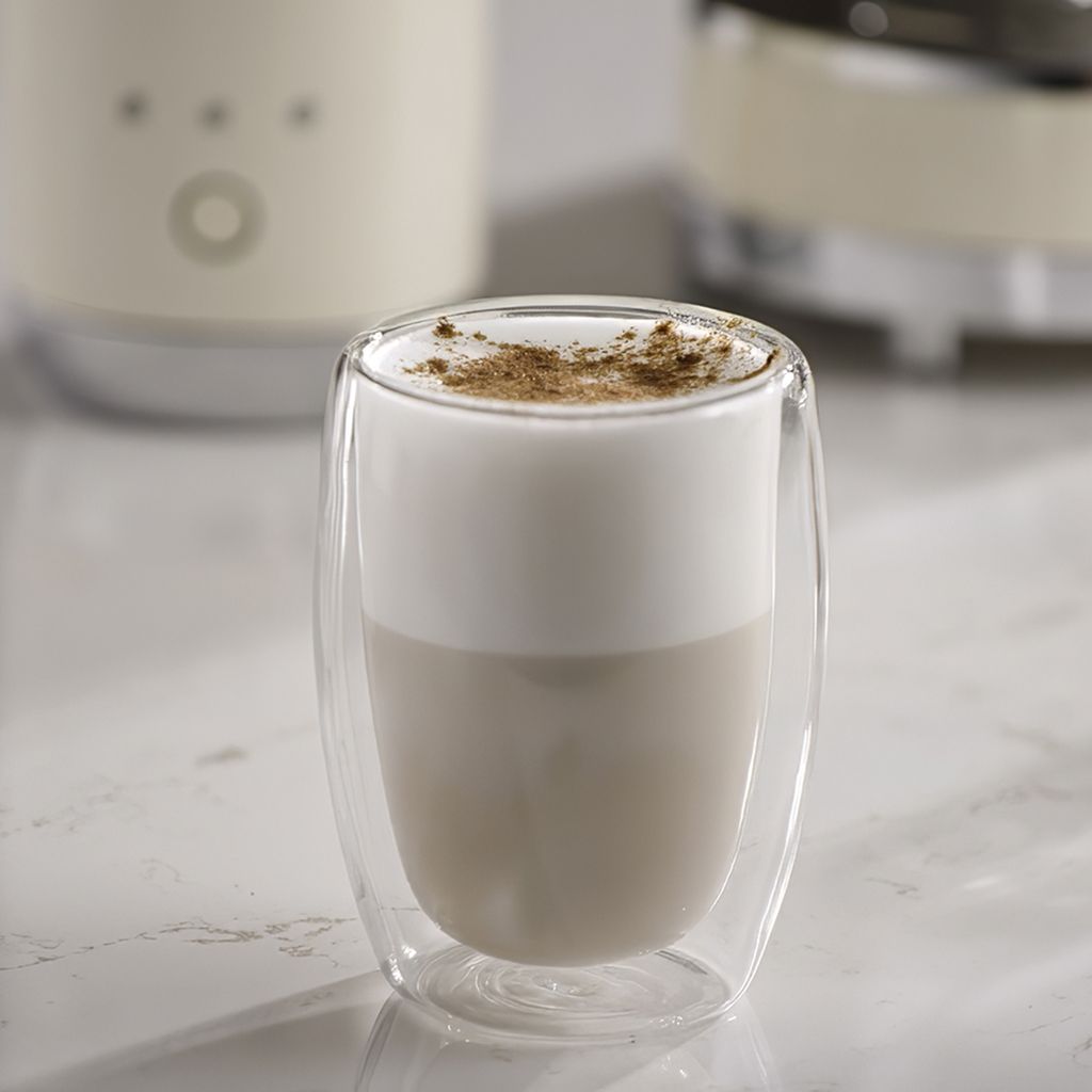 A layered iced cappuccino served in a double-walled glass, with creamy foam topped with a light dusting of cocoa