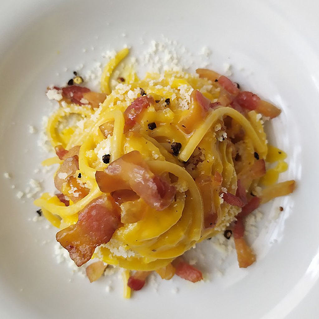 Top-down view of spaghetti carbonara with creamy egg sauce, crispy guanciale, grated cheese, and black pepper.