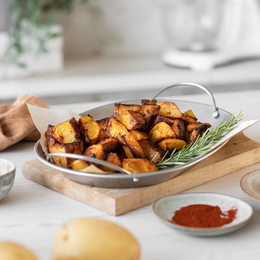 Golden-brown roasted potato wedges in a black pan, topped with red chili slices and fresh parsley.