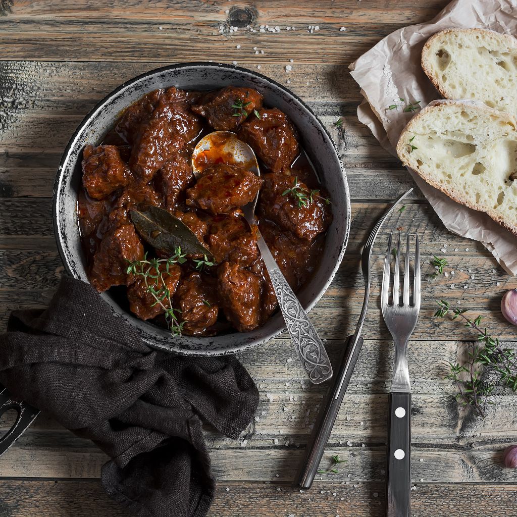 Slow-cooked braised beef in a rich red wine sauce served in a dark bowl alongside crusty bread slices on a wooden table.